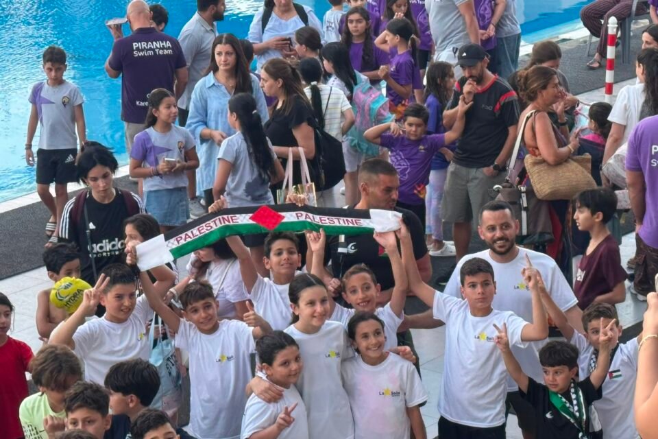 De La Salle swimmers, coaches, and families celebrating together beside the pool with a Palestine scarf.