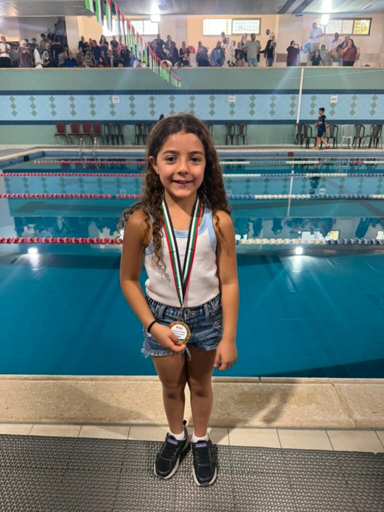 Young medal-winning swimmer standing beside the championship pool.