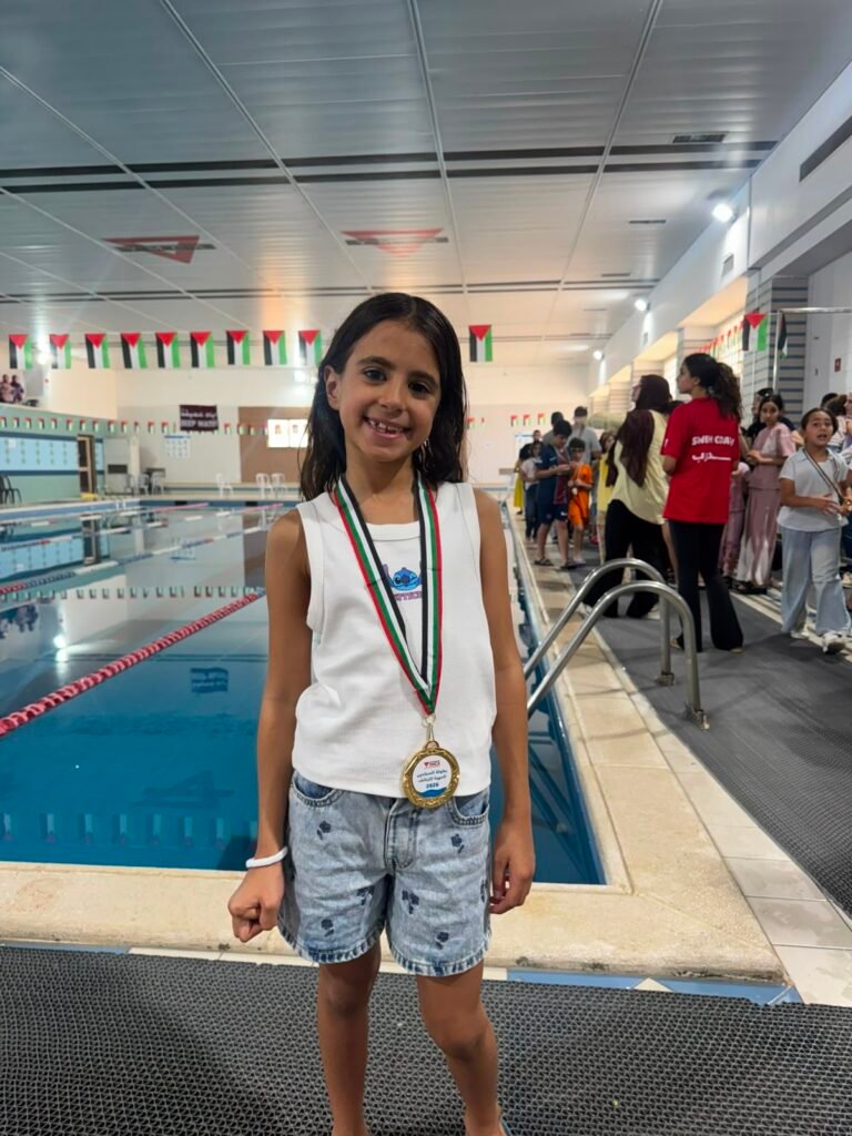 Young medal-winning swimmer standing proudly beside the championship pool.
